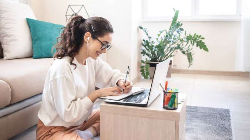 Deutsch Online lernen von zuhause: Frau schreibt Notizen am Laptop im Wohnzimmer